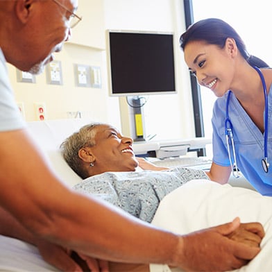 Smiling female medical practitioner attends to smiling patient in hospital bed Smiling female medical practitioner attends to smiling patient in hospital bed